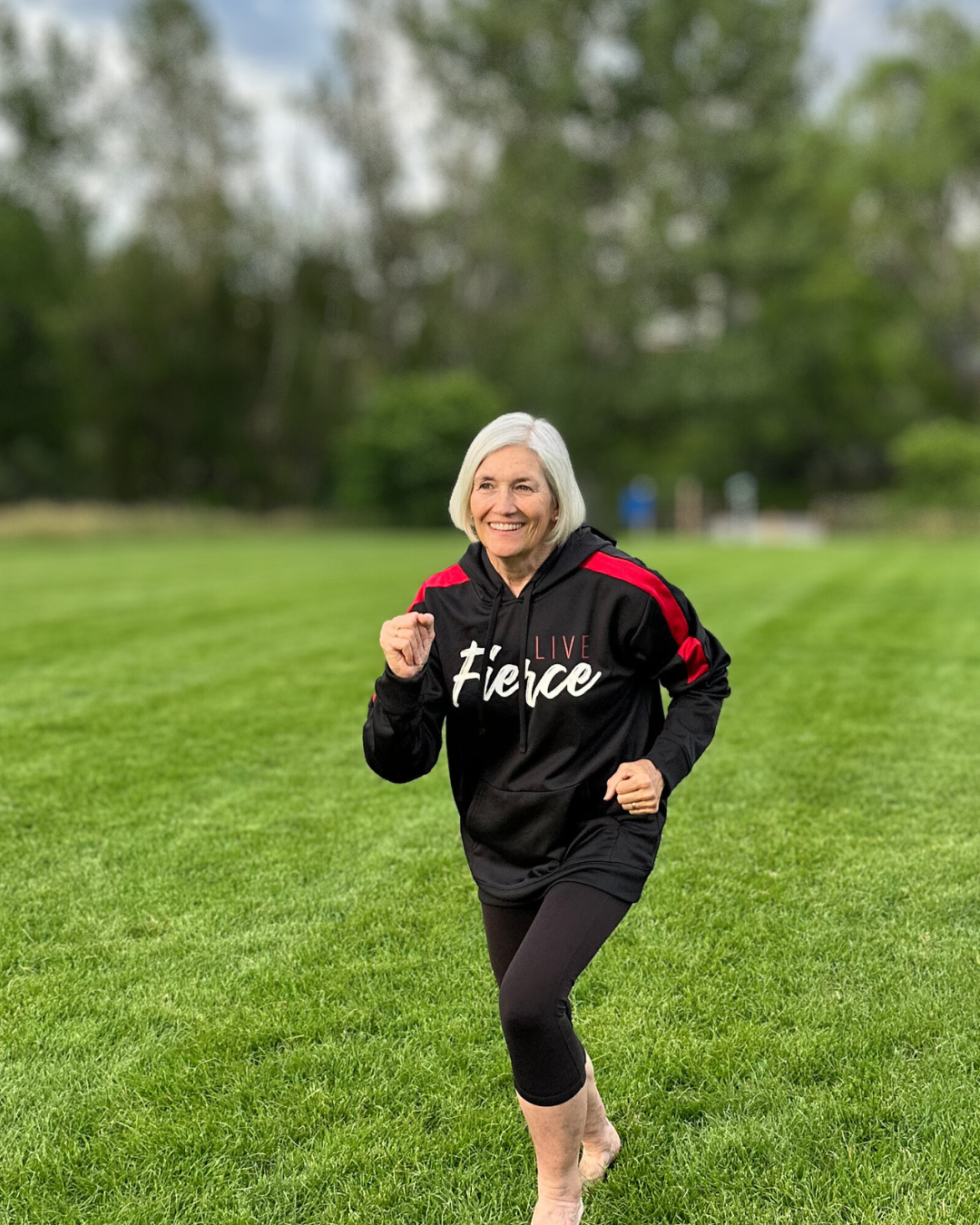 Image of a woman wearing black Live Fierce Hoodie while running on grass.