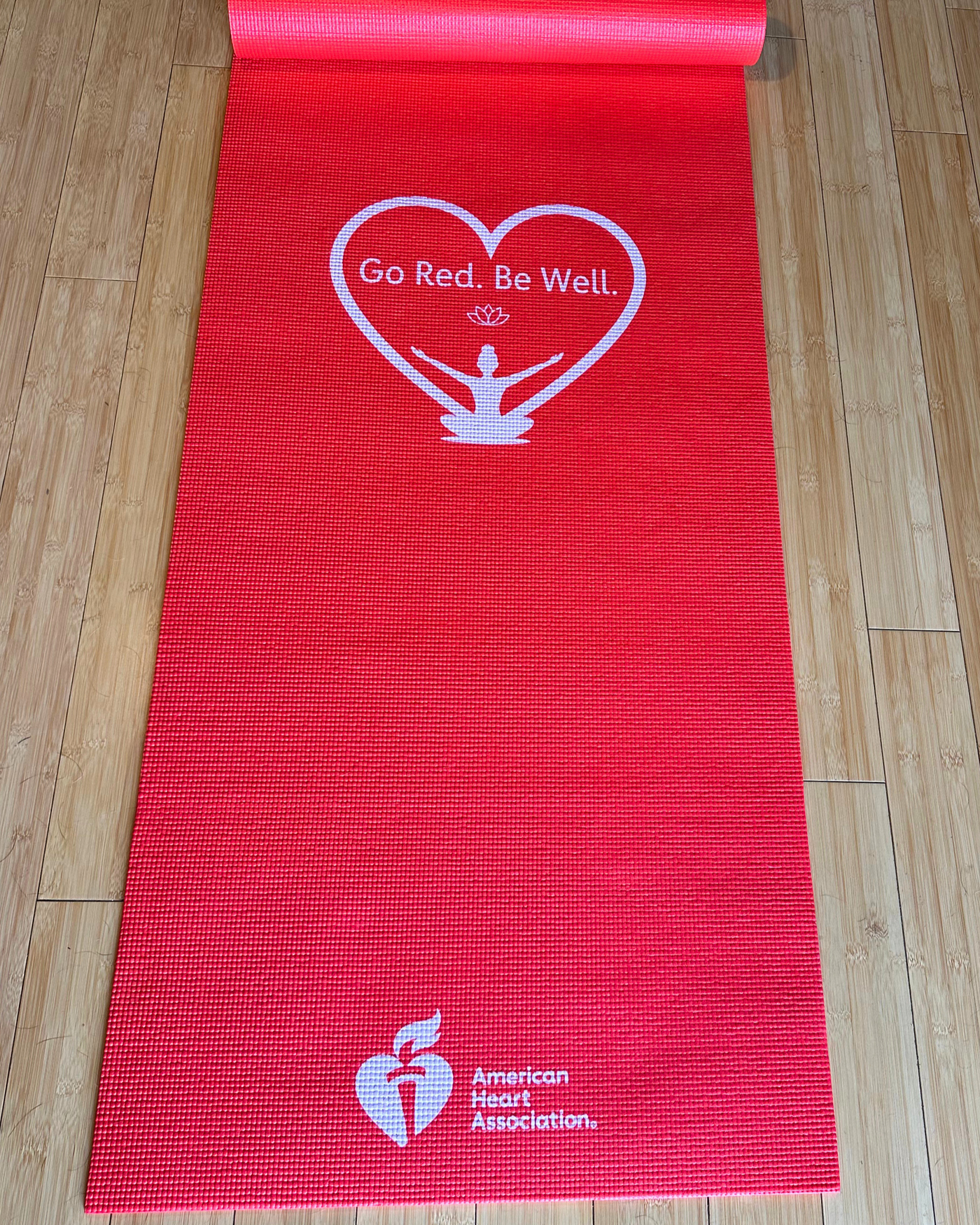 Picture showing unrolled yoga mat with Go Red. Be Well Logo and AHA logo on red mat.